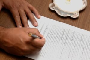 Home Hand signing a contract on a wooden desk, emphasizing business formalities.
