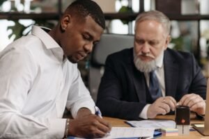 Home Two businessmen collaborating in an office setting, focused on document review and strategic planning.
